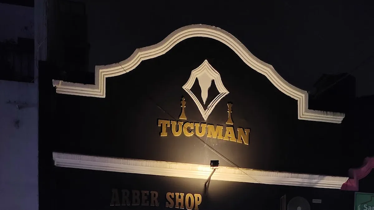 Frente de Tucumán Barbershop de noche, con el cartel dorado iluminado